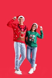 Beautiful happy couple in Santa hats and Christmas sweaters on red background