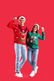 Photo of Beautiful happy couple in Santa hats and Christmas sweaters on red background