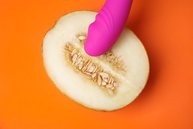Photo of Half of melon and purple vibrator on orange background, flat lay. Sex concept