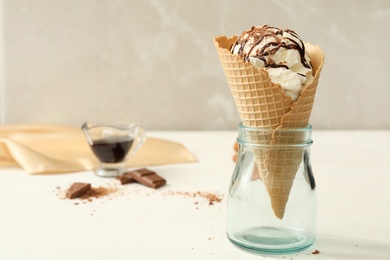 Delicious vanilla ice cream with toppings in wafer cone on white wooden table. Space for text