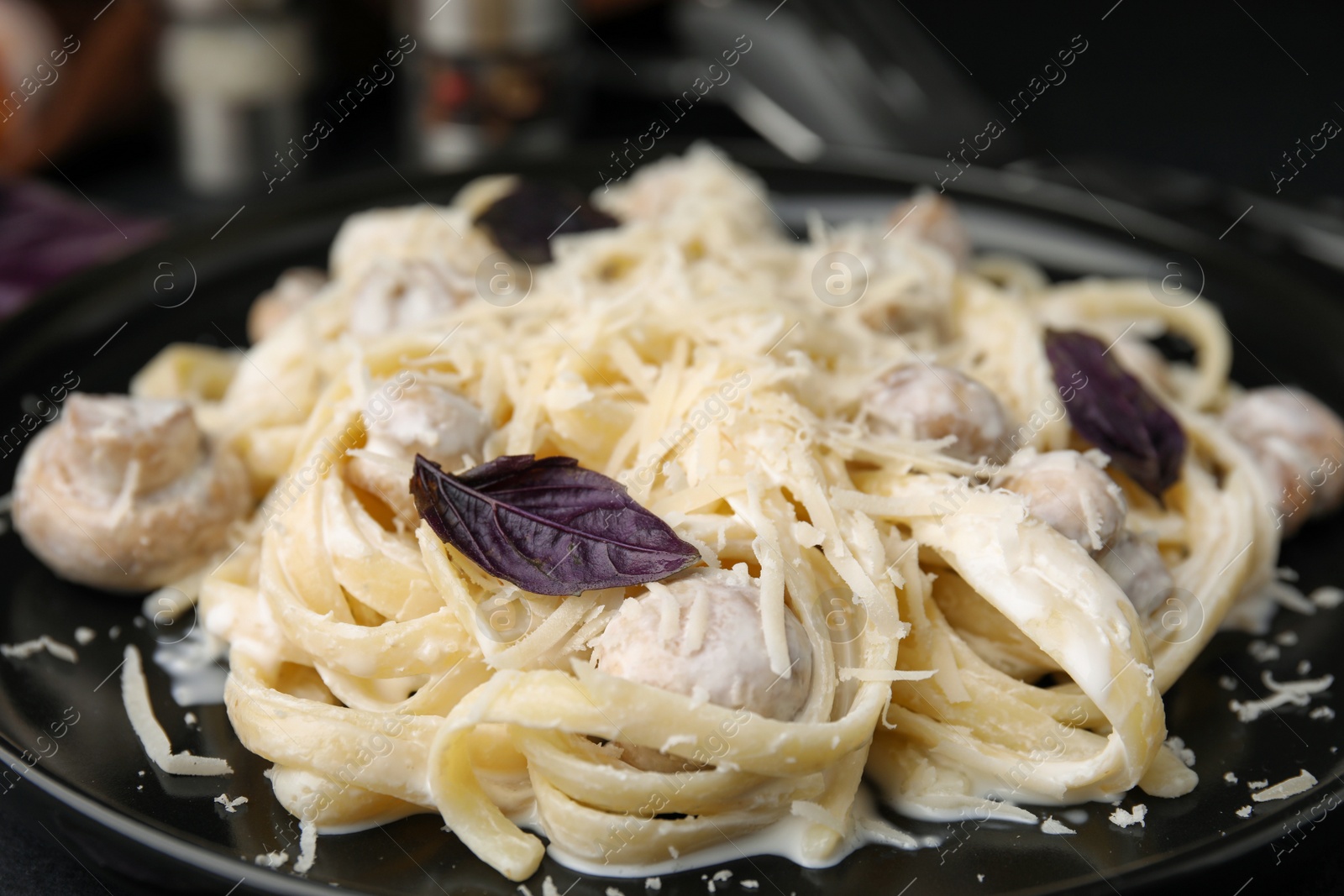 Photo of Delicious pasta with mushrooms on black plate, closeup