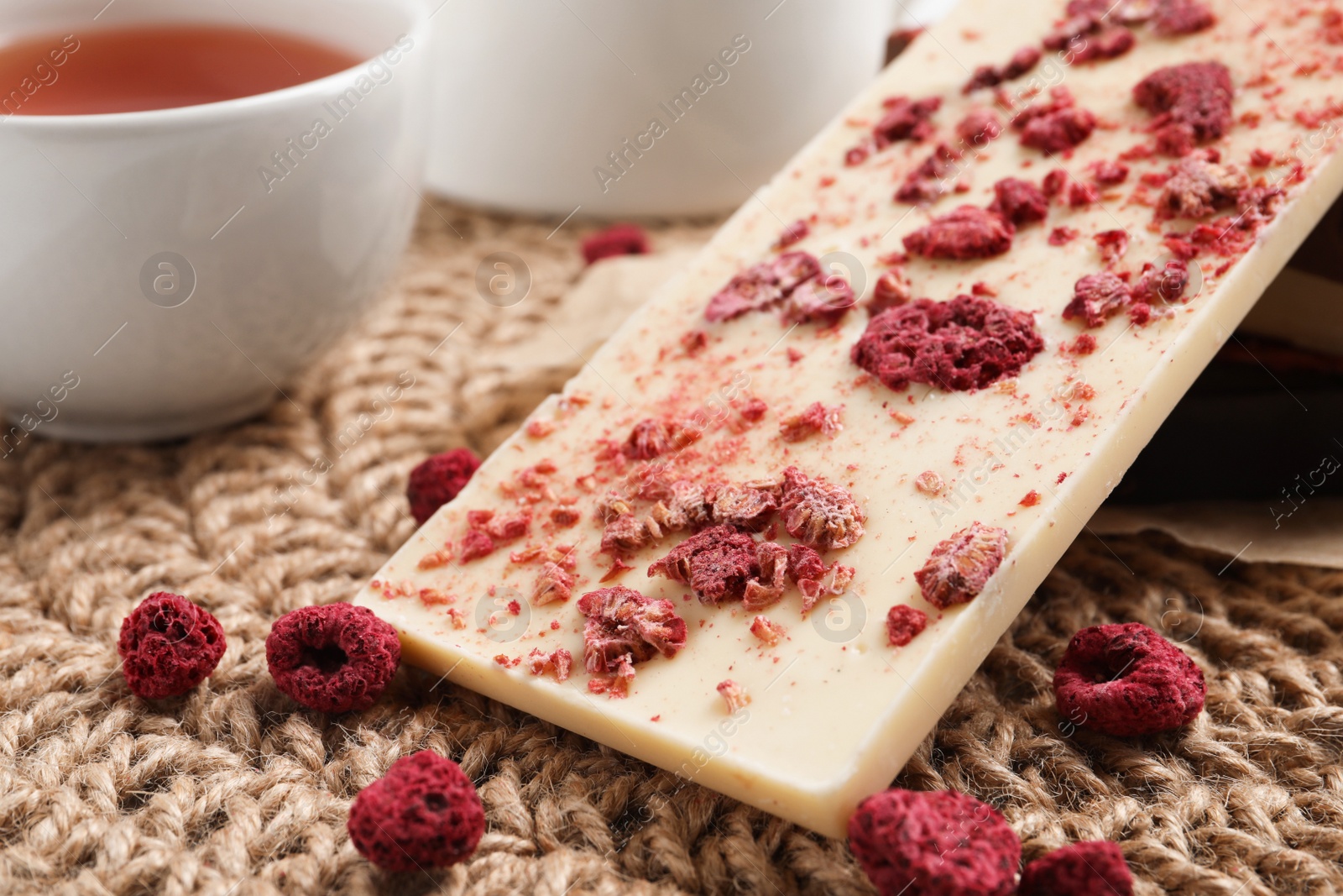 Photo of Chocolate bar with freeze dried fruits on wicker mat, closeup