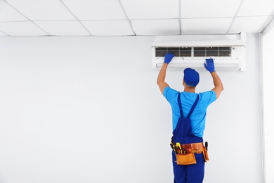 Photo of Professional technician maintaining modern air conditioner indoors. Space for text