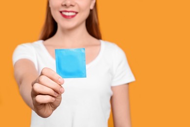 Photo of Woman holding condom on yellow background, closeup and space for text. Safe sex