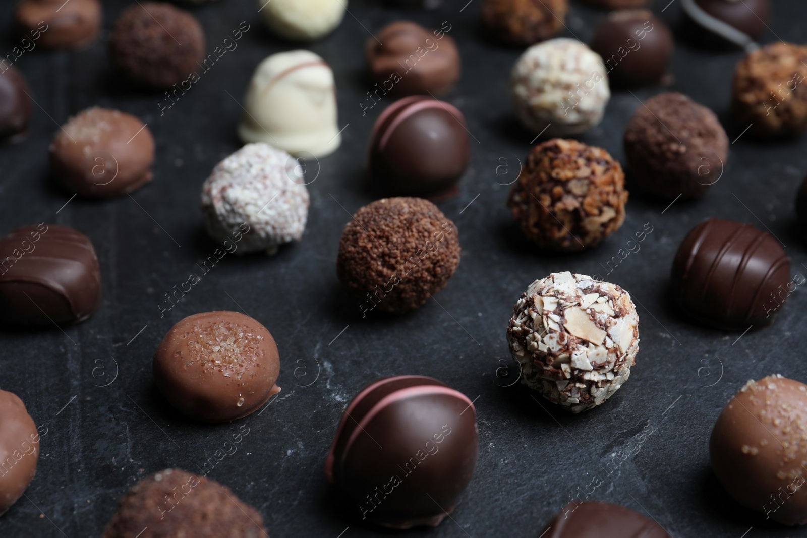 Photo of Different delicious chocolate candies on black table, closeup