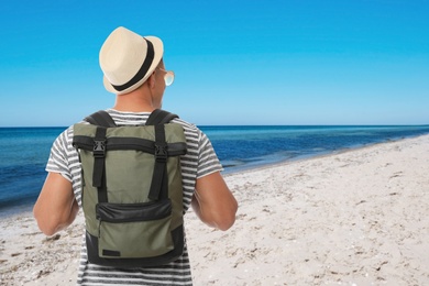 Traveler with backpack on sandy beach during summer vacation trip, back view. Space for text