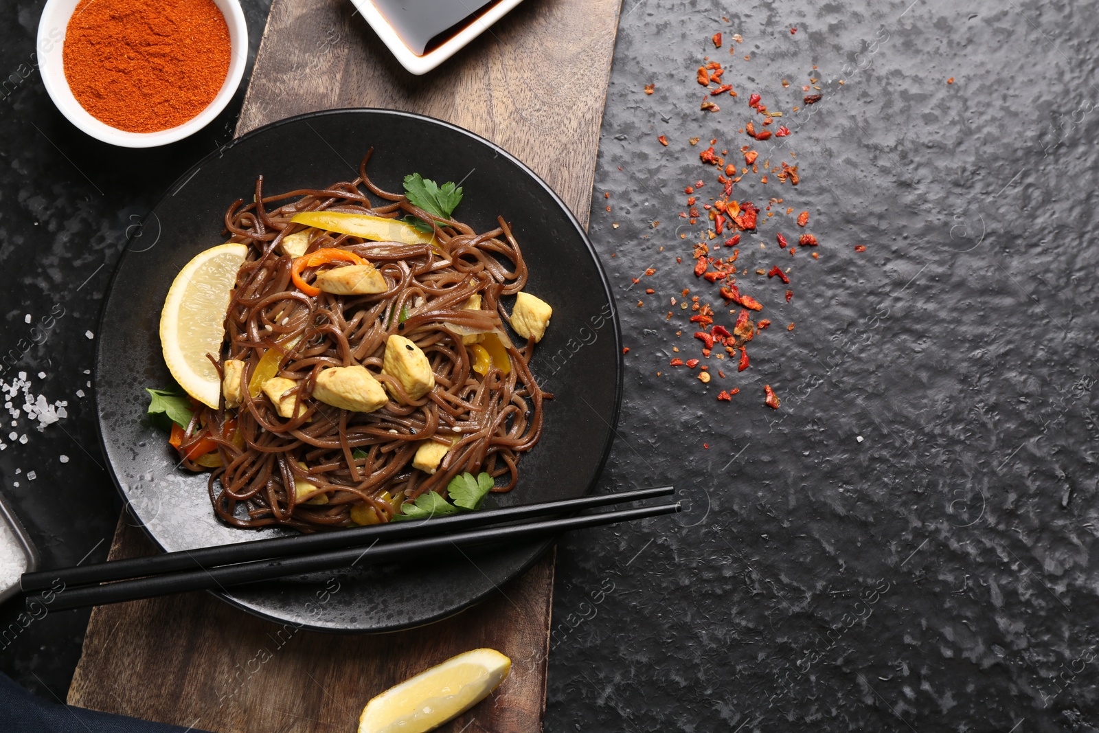 Photo of Stir-fry. Tasty noodles with vegetables and meat served on dark textured table, flat lay. Space for text