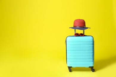 Stylish blue suitcase with hat and sunglasses on yellow background. Space for text
