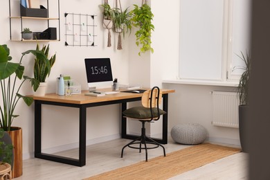 Cozy workplace with computer, modern furniture and houseplants at home