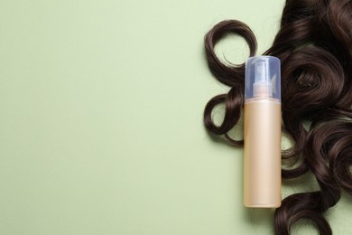 Photo of Spray bottle with thermal protection and lock of brown hair on pale green background, flat lay. Space for text