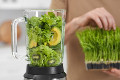 Man holding microgreen peas for delicious smoothie and blender with ingredients indoors, closeup