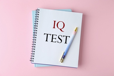 Notebook with text IQ Test and pen on pink background, top view