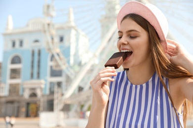 Young happy woman eating ice cream in amusement park. Space for text