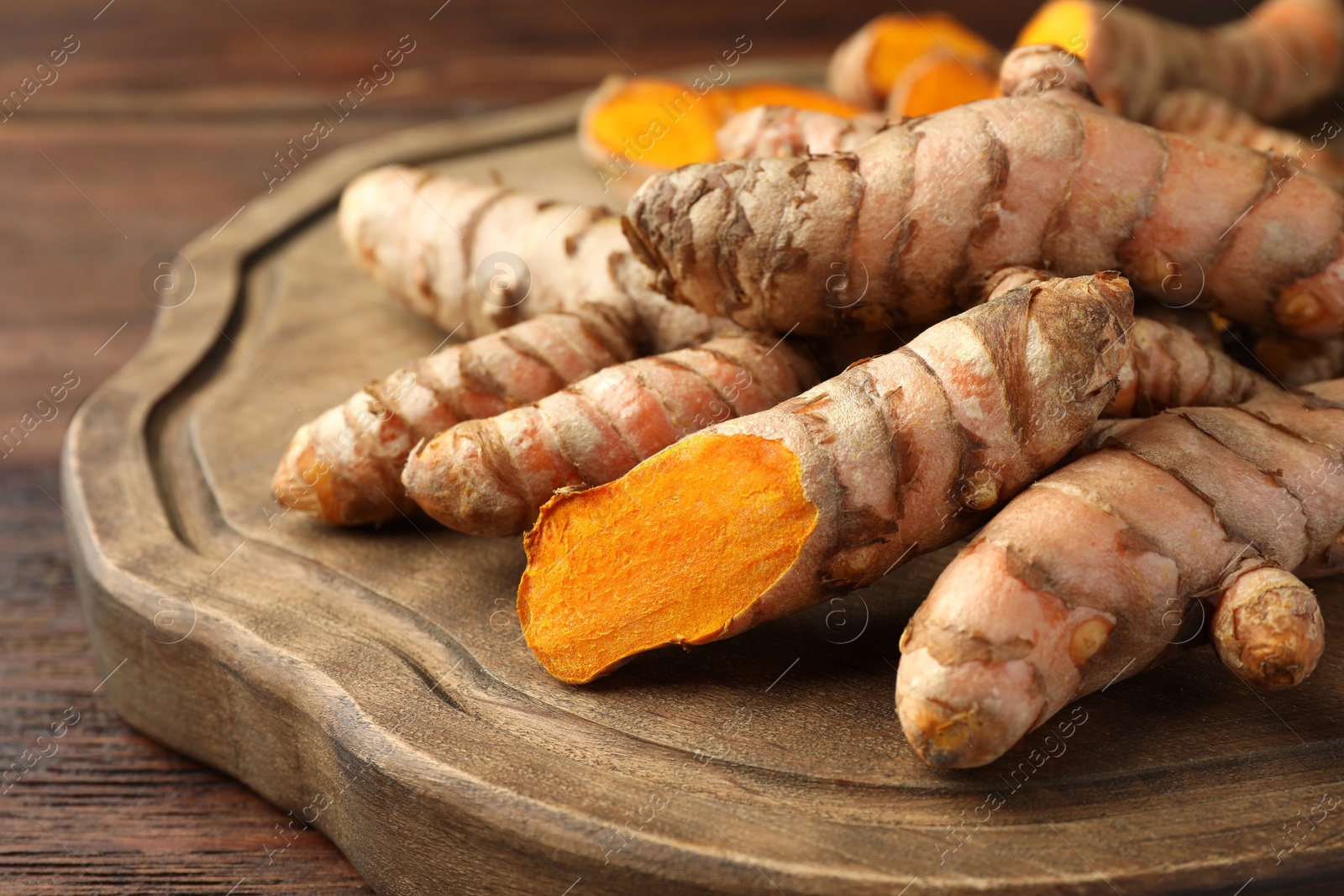 Photo of Many fresh turmeric roots on wooden board, closeup