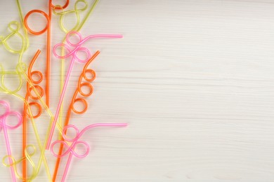 Photo of Colorful plastic drinking straws on white wooden table, flat lay. Space for text