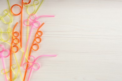 Colorful plastic drinking straws on white wooden table, flat lay. Space for text