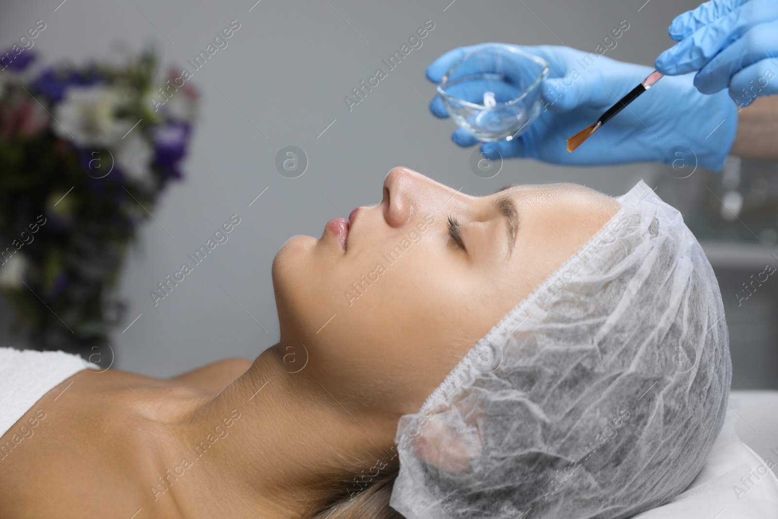 Photo of Cosmetologist applying chemical peel product on client's face in salon