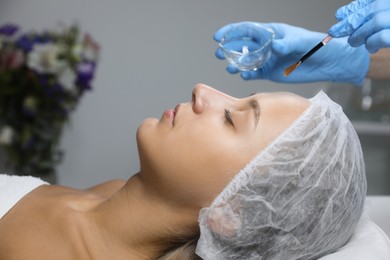 Cosmetologist applying chemical peel product on client's face in salon