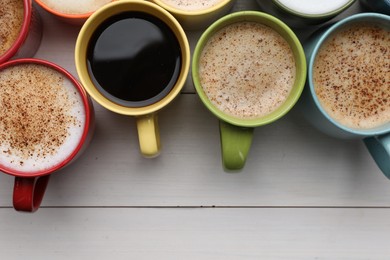 Many different cups with aromatic hot coffee on white wooden table, flat lay