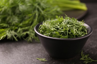 Photo of Fresh cut dill in bowl on dark textured table, closeup