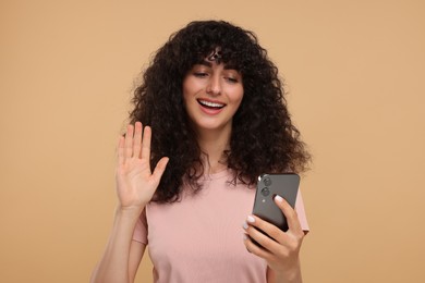 Photo of Happy young woman looking at smartphone and waving hello on beige background