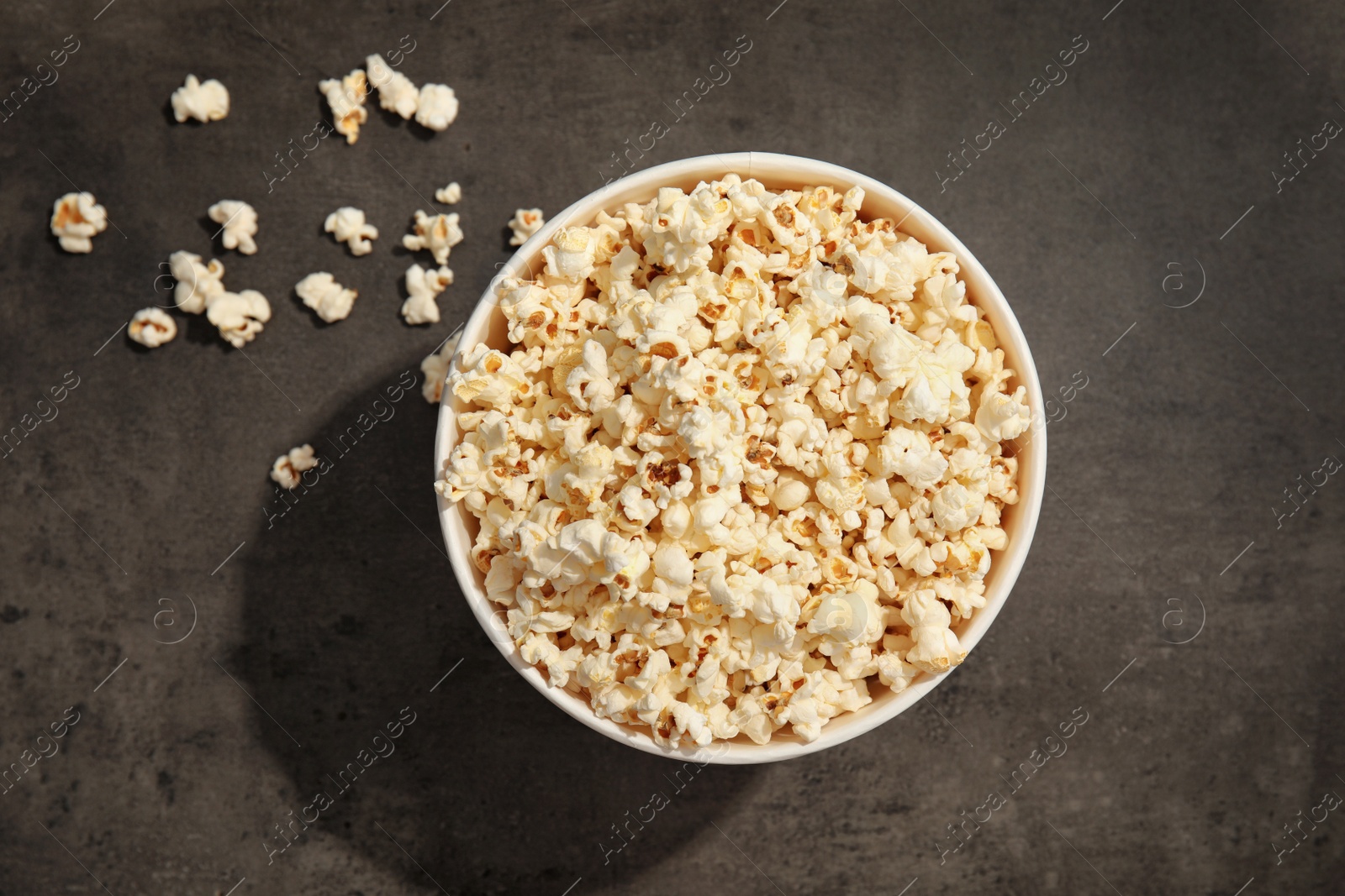 Photo of Paper bucket of tasty popcorn on grey background, top view