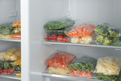 Plastic bags with different frozen vegetables in refrigerator