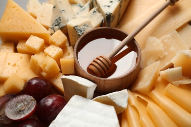 Different types of delicious cheese, grapes and honey as background, closeup