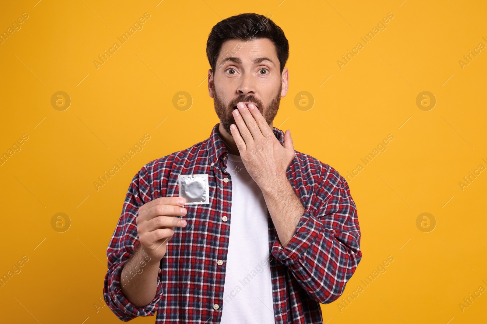 Photo of Emotional man holding condom on yellow background. Safe sex