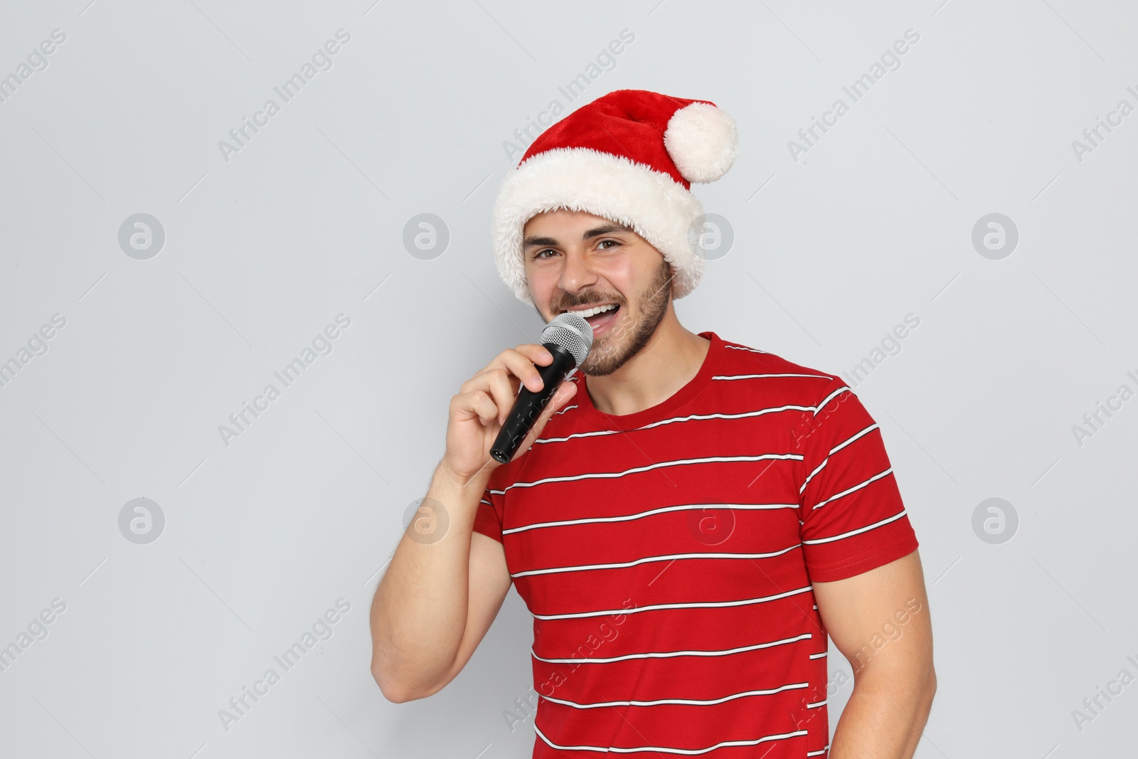 Photo of Young man in Santa hat singing into microphone on color background. Christmas music