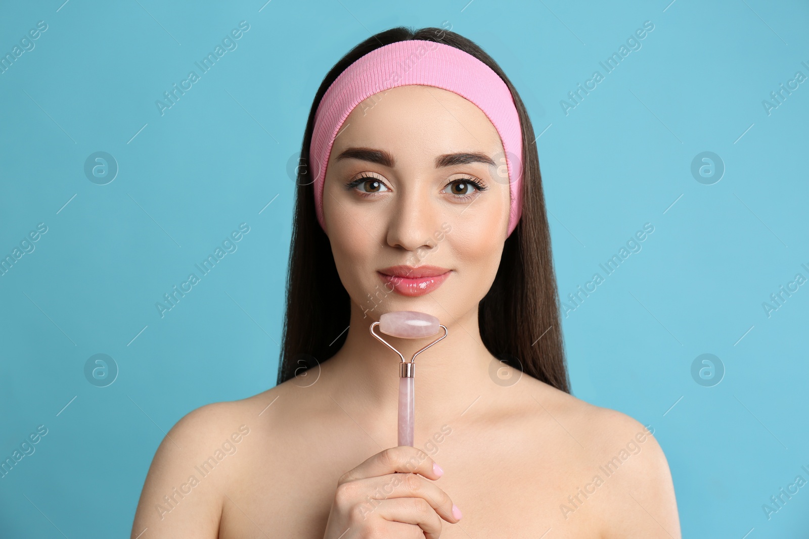 Photo of Woman using natural face pink quartz roller on light blue background