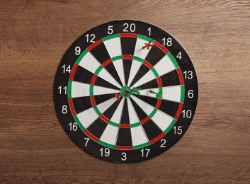 Dart board with color arrows on wooden background, top view