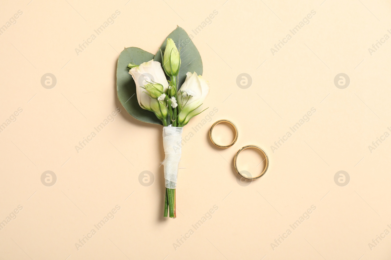 Photo of Wedding stuff. Stylish boutonniere and rings on beige background, top view