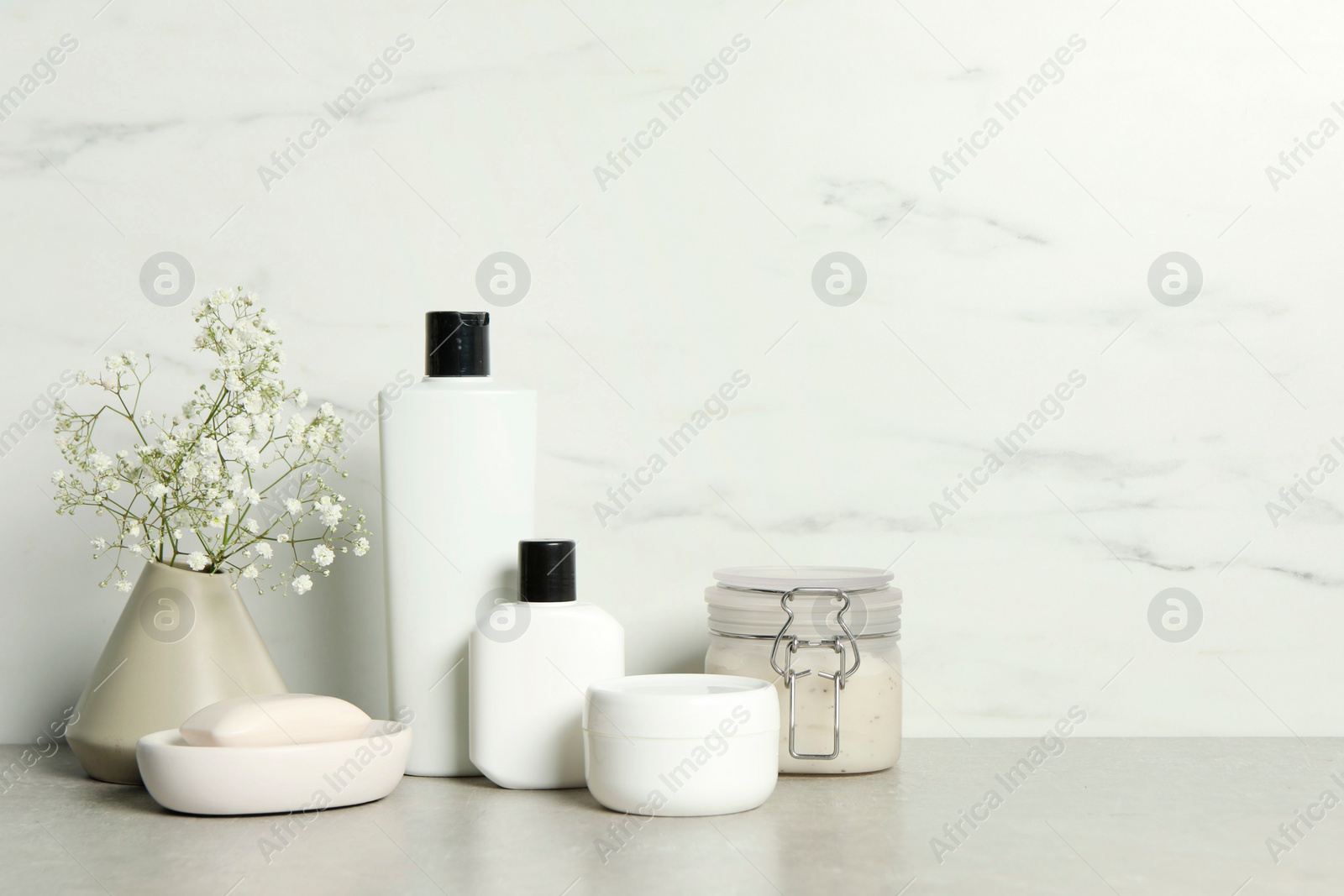 Photo of Bath accessories. Personal care products and gypsophila flowers in vase on gray table near white marble wall, space for text