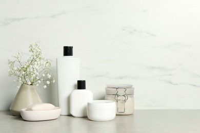 Bath accessories. Personal care products and gypsophila flowers in vase on gray table near white marble wall, space for text