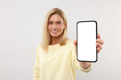 Photo of Happy woman holding smartphone with blank screen on white background, selective focus