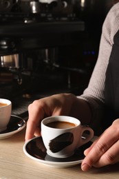 Photo of Barista with cup of fresh aromatic coffee at wooden counter in cafe, closeup