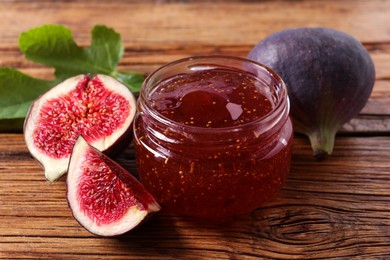 Jar of tasty sweet jam and fresh figs on wooden table, closeup