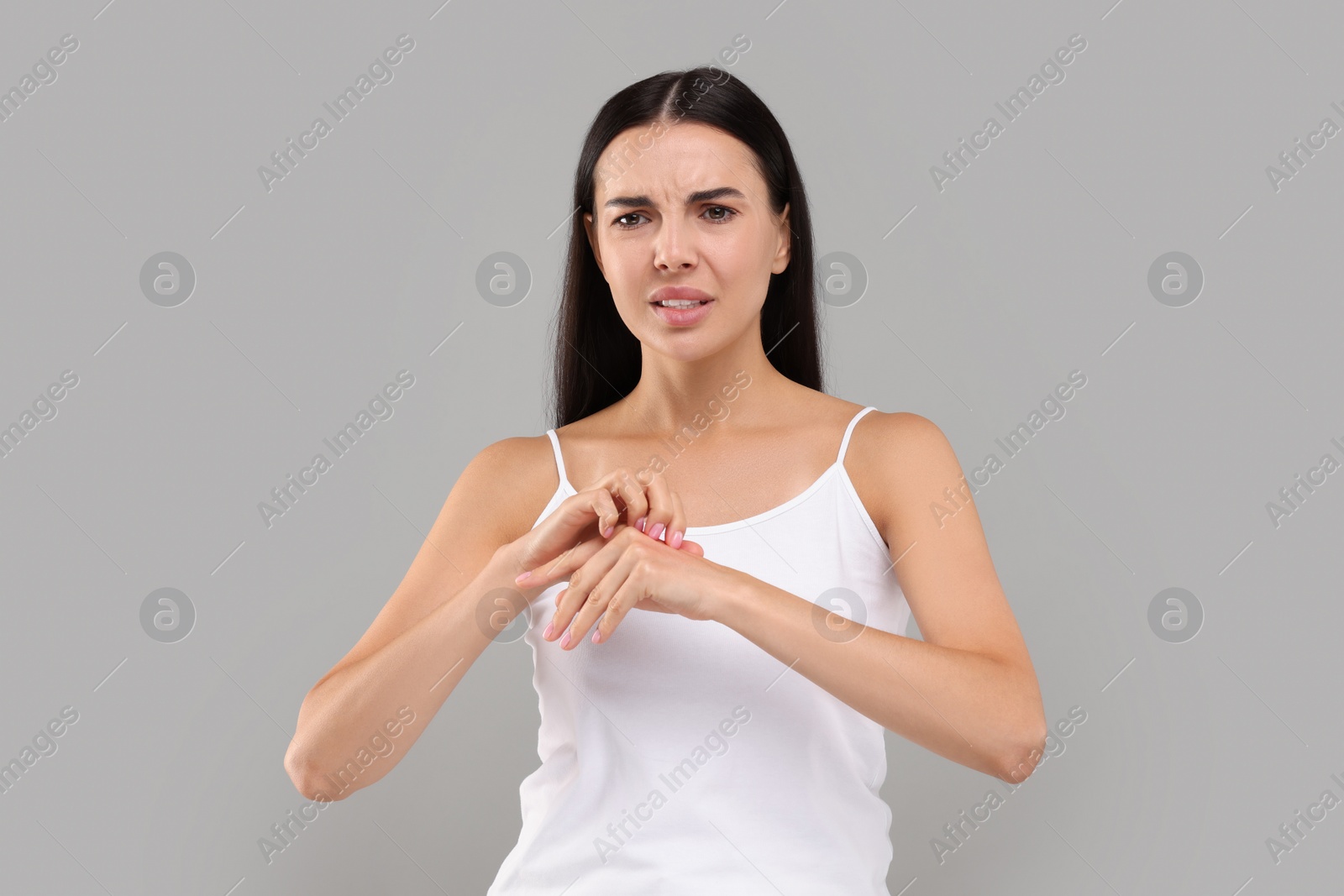 Photo of Suffering from allergy. Young woman scratching her hand on light grey background