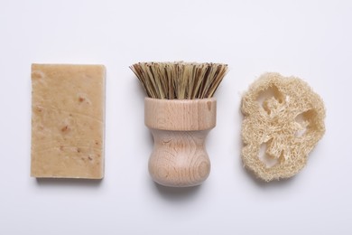 Photo of Cleaning brush, soap bar and loofah on white background, flat lay