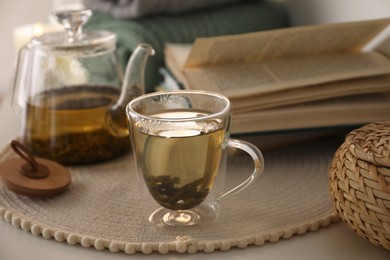 Photo of Glass teapot and cup of hot tea on table in room. Cozy home atmosphere