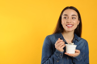 Happy woman with tasty yogurt on orange background. Space for text