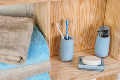 Photo of Dish with soap, bottle of shampoo and toothbrushes on wooden shelf