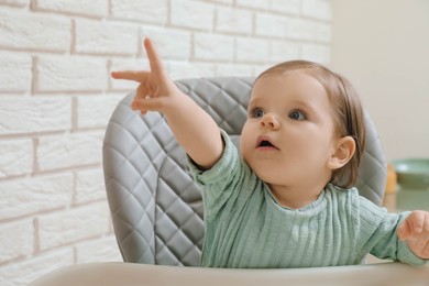 Cute little baby pointing at something in high chair indoors