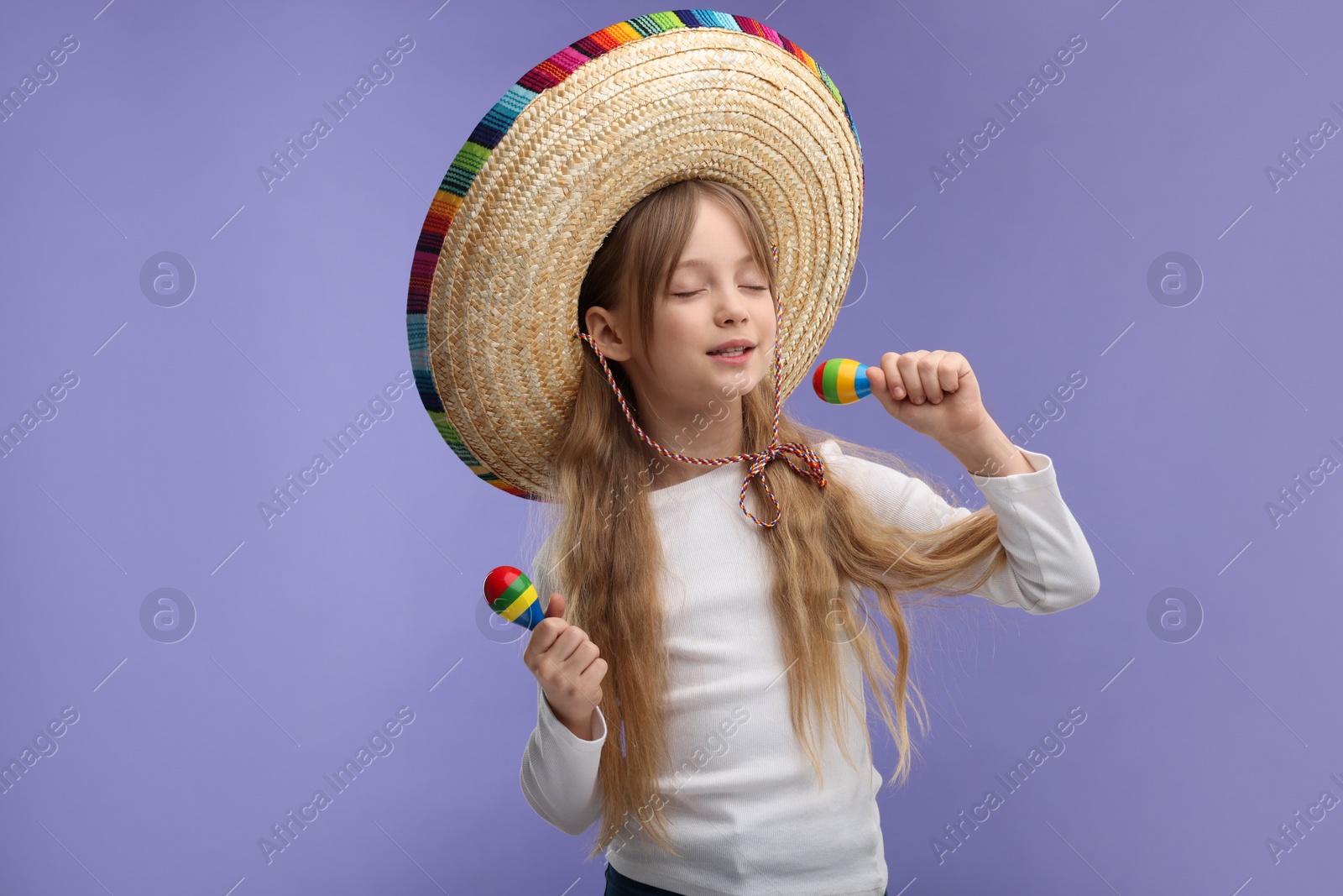 Photo of Cute girl in Mexican sombrero hat singing with maracas on purple background