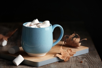 Cup of hot cozy drink with marshmallows and autumn leaves on table. Space for text