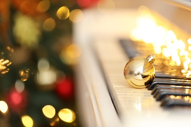 Photo of Beautiful golden bauble and fairy lights on piano keys, space for text. Christmas music