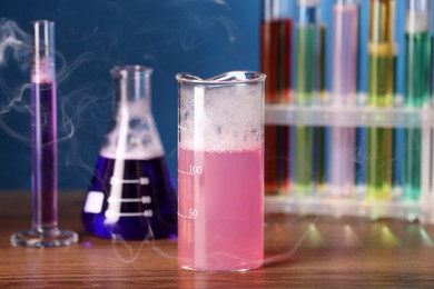 Laboratory glassware with colorful liquids and steam on wooden table. Chemical reaction