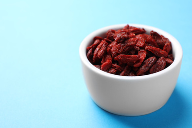 Photo of Dried goji berries in bowl on light blue background, closeup. Space for text