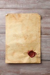 Sheet of old parchment paper with wax stamp on wooden table, top view